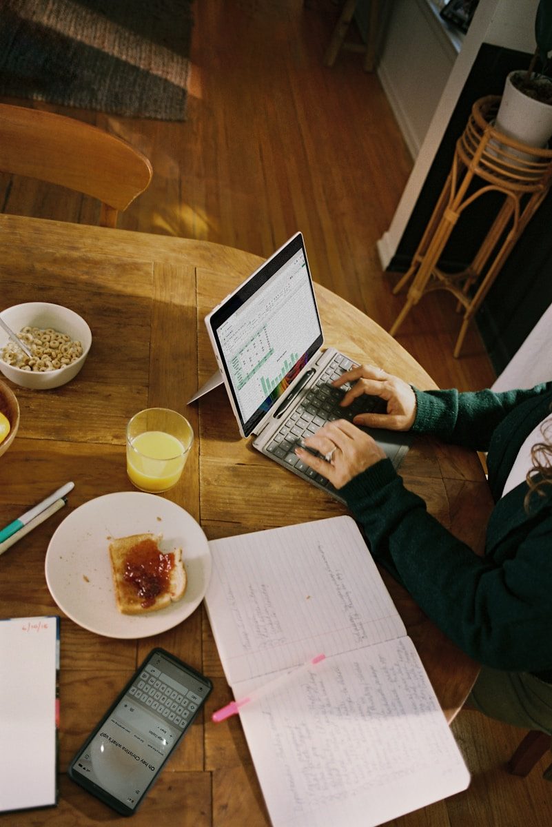 Person working on laptop at wooden table with breakfast.